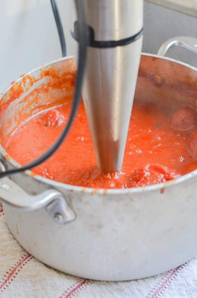 Using immersion blender to blend tomato soup smooth.