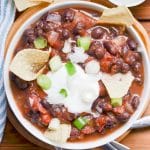 black bean chili in bowl with sour cream, chopped green onions and corn chips.