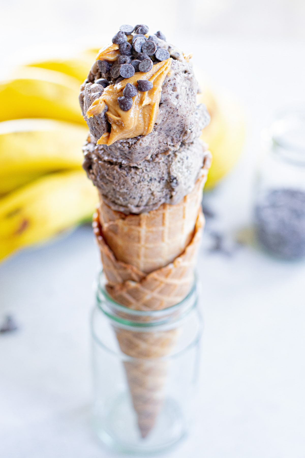 peanut butter banana ice cream in a cone with drizzle of peanut butter and chocolate chps.