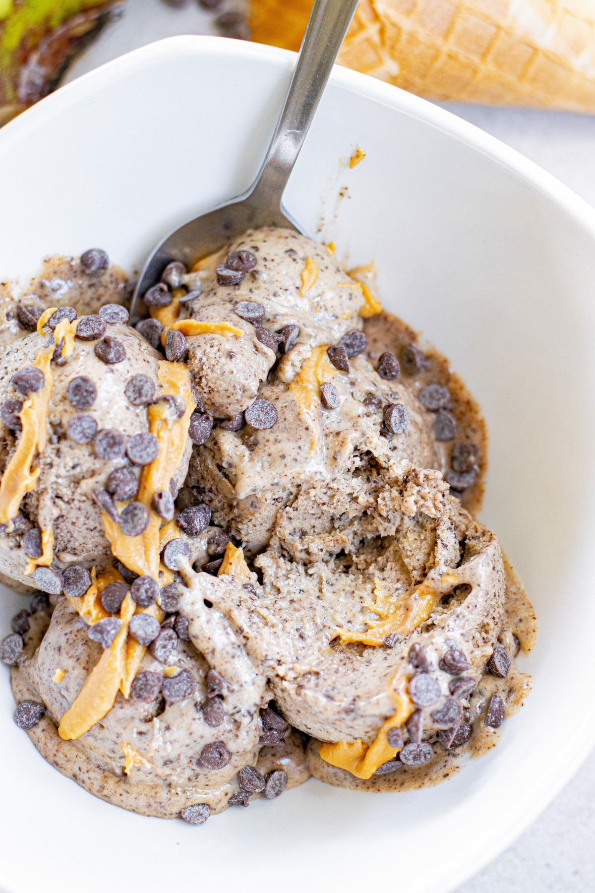 scoops of banana ice cream in a bowl with peanut butter drizzles and chocolate chips.