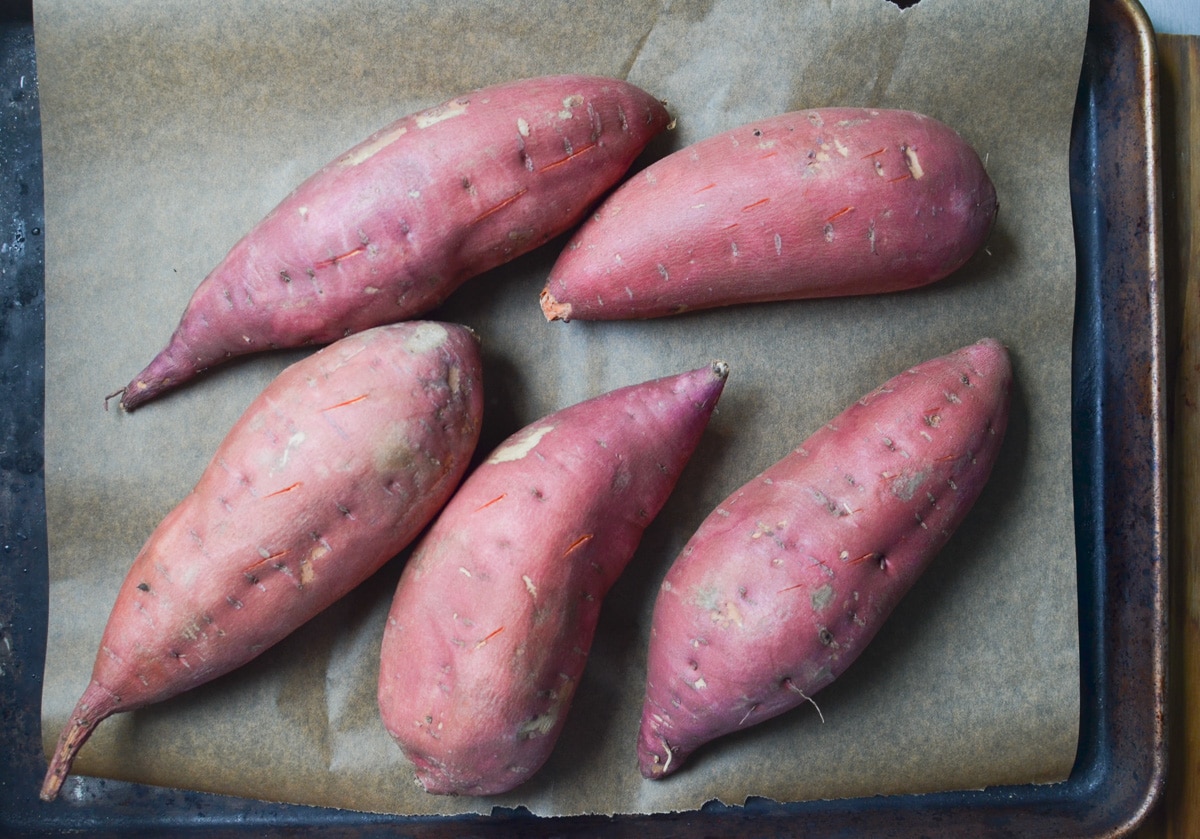 five sweet potatoes on a baking sheet.