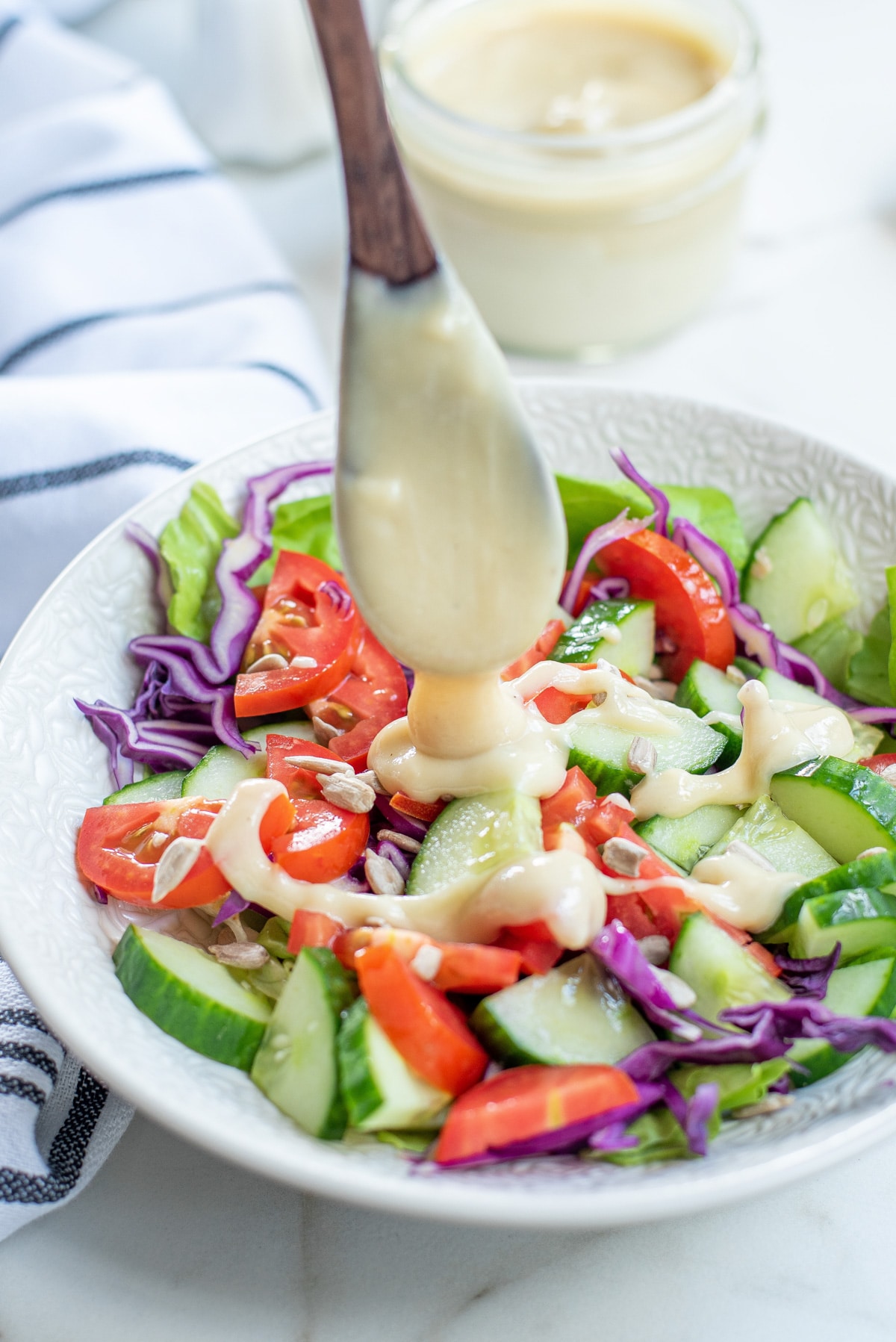 pouring tahini dressing on green salad.