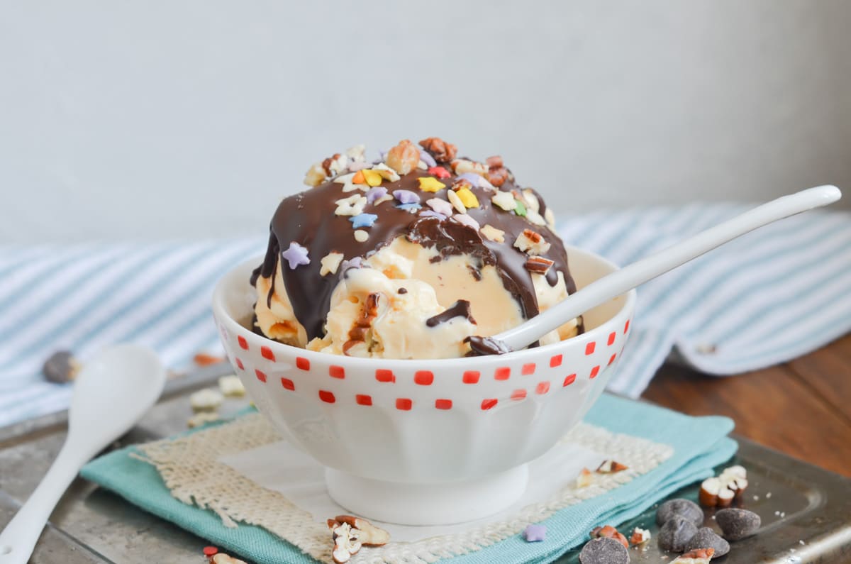 chocolate shell drizzled on vanilla ice cream in bowl with chopped nuts and sprinkles.