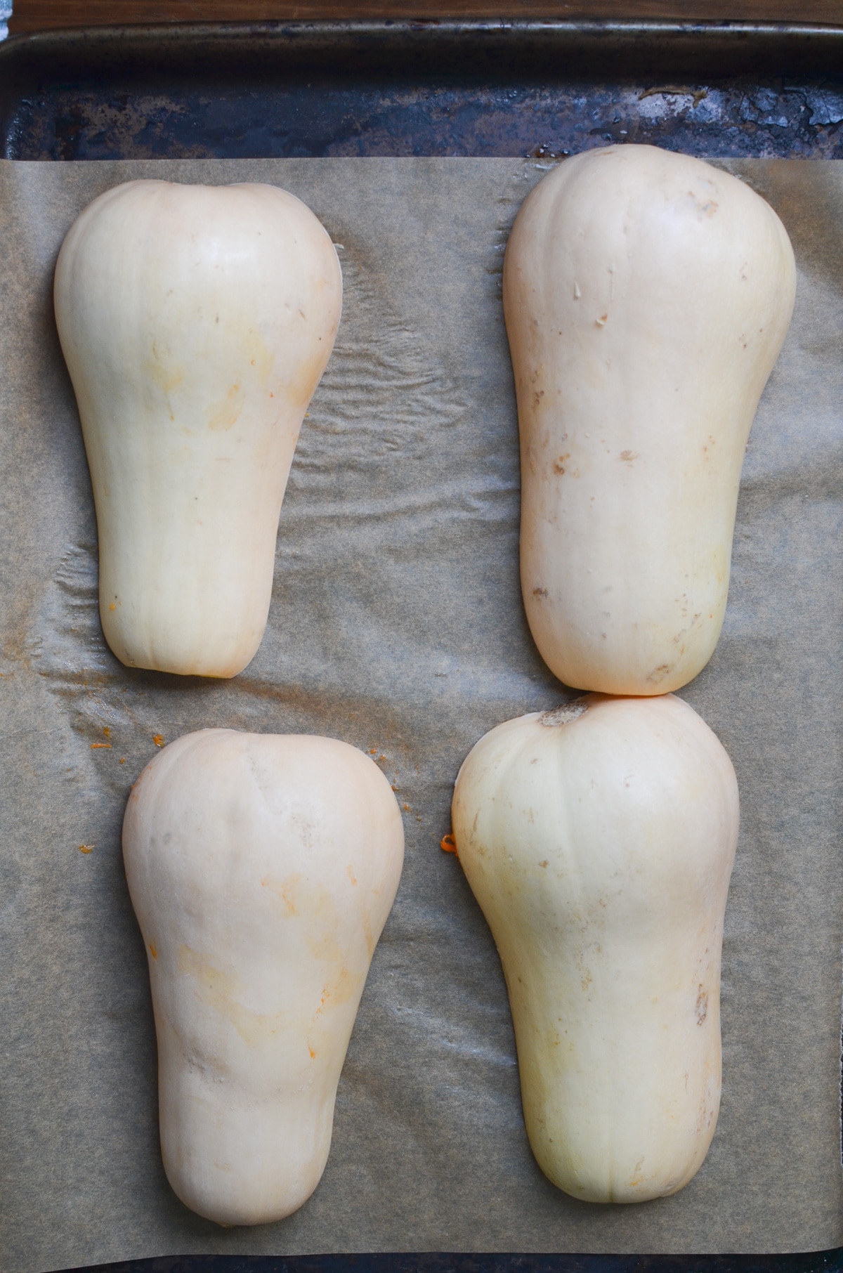 two butternut squashes cut in half on baking sheet.