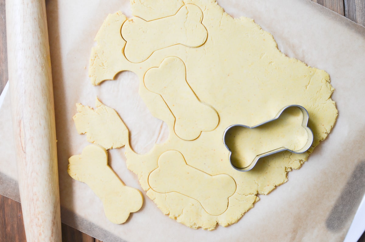 Peanut butter dog treats dough rolled out and biscuits being made with dog bone cookie cutter.