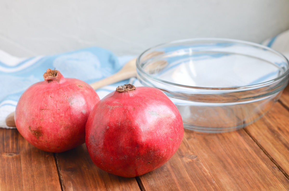 Two pomegranates next to a bowl.