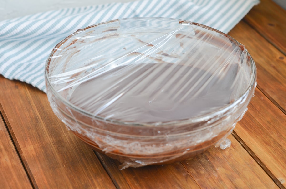 melted chocolate and coconut cream in mixing bowl with plastic wrap.