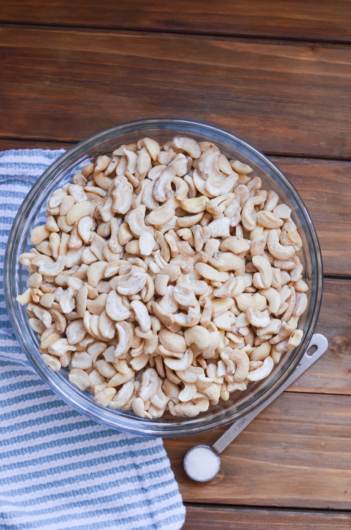 Raw cashews in a glass bowl with 1/4 teaspoon of salt.