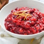 Paleo cranberry sauce in bowl with orange garnish on counter.