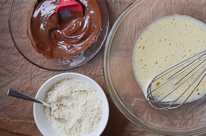 eggs whisked in mixing bowl, bowl of dry ingredients, bowl of melted chocolate on counter.