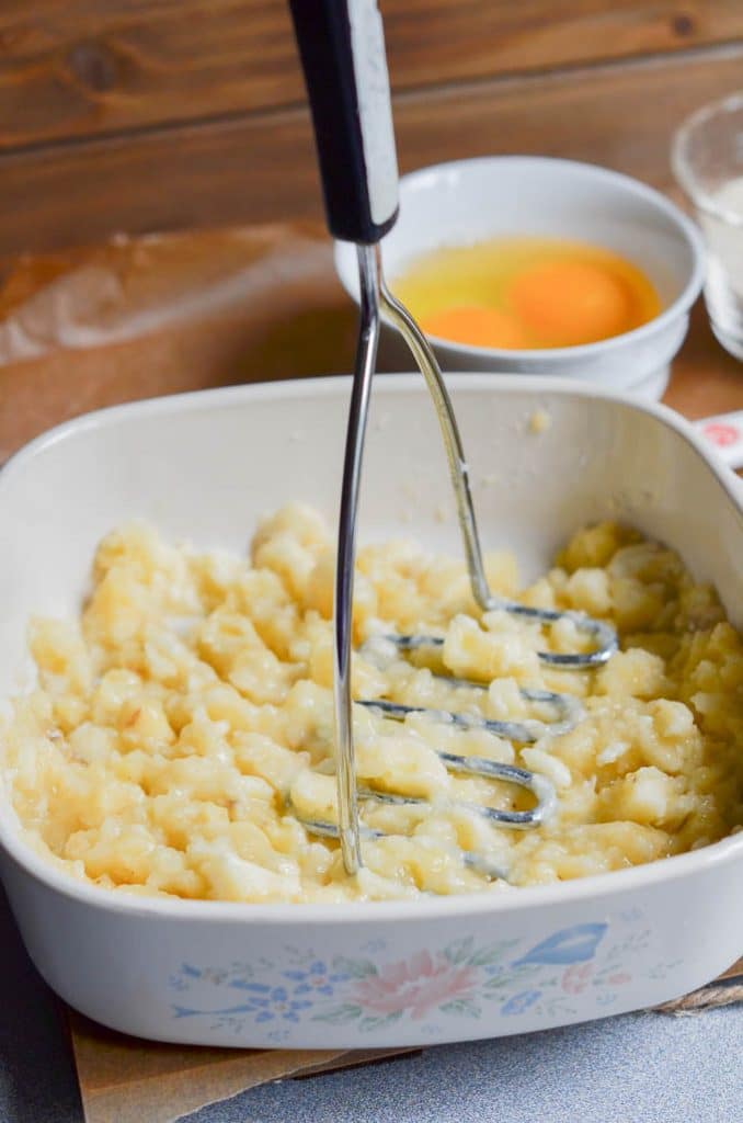 Pureeing banana in dish with potato masher.