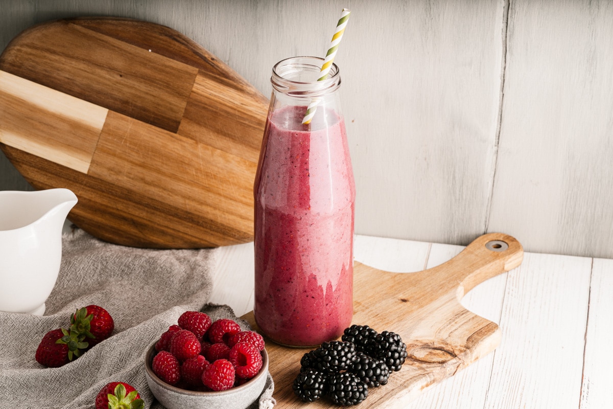 Smoothie in glass jar with berries on cutting board.