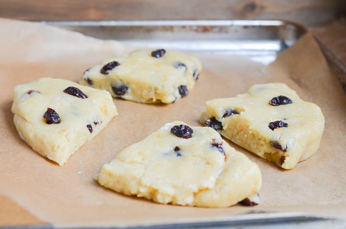 Paleo scones dough cut into four pieces on baking sheet pan.