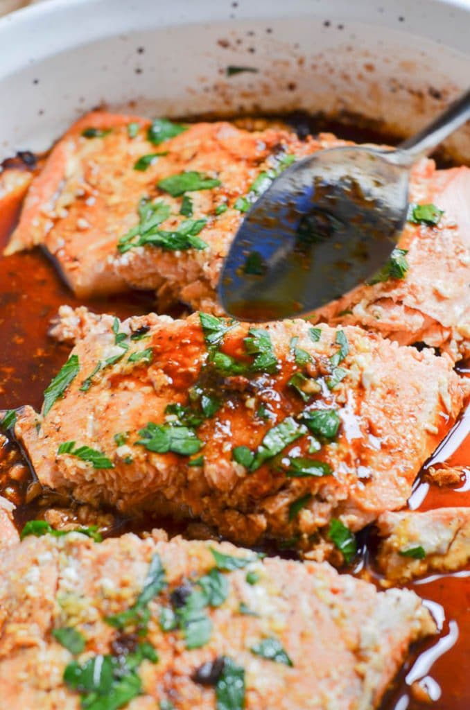 pouring more glaze over salmon in casserole dish.