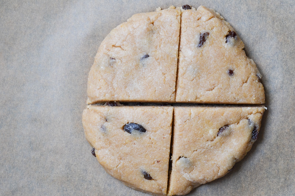 Gluten-free cinnamon raisin scone dough shaped into a round cut into four slices.