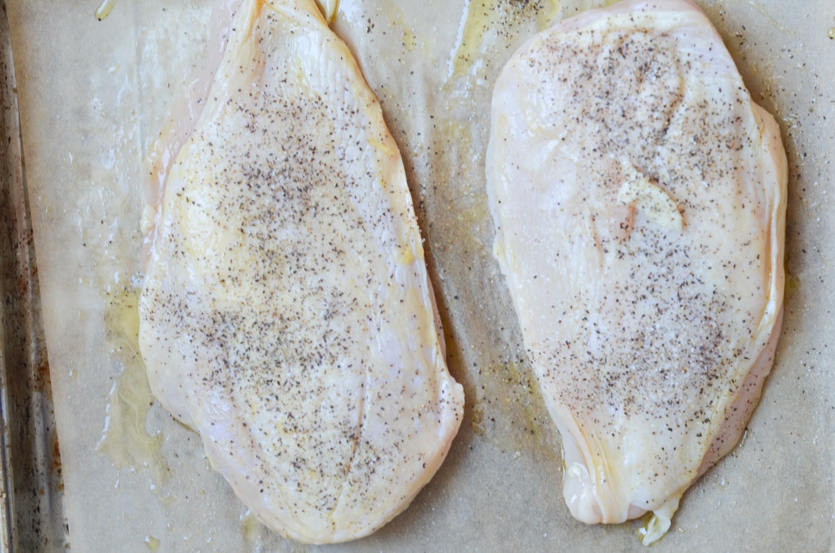 two chicken breast coated with olive oil and salt and pepper.