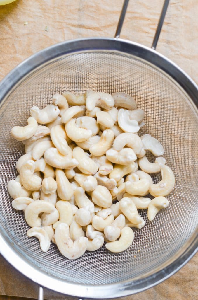 Cashews being drained and rinsed through metal strainer.