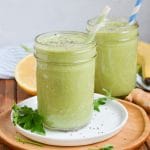 two green detox smoothies in glasses on white plate.