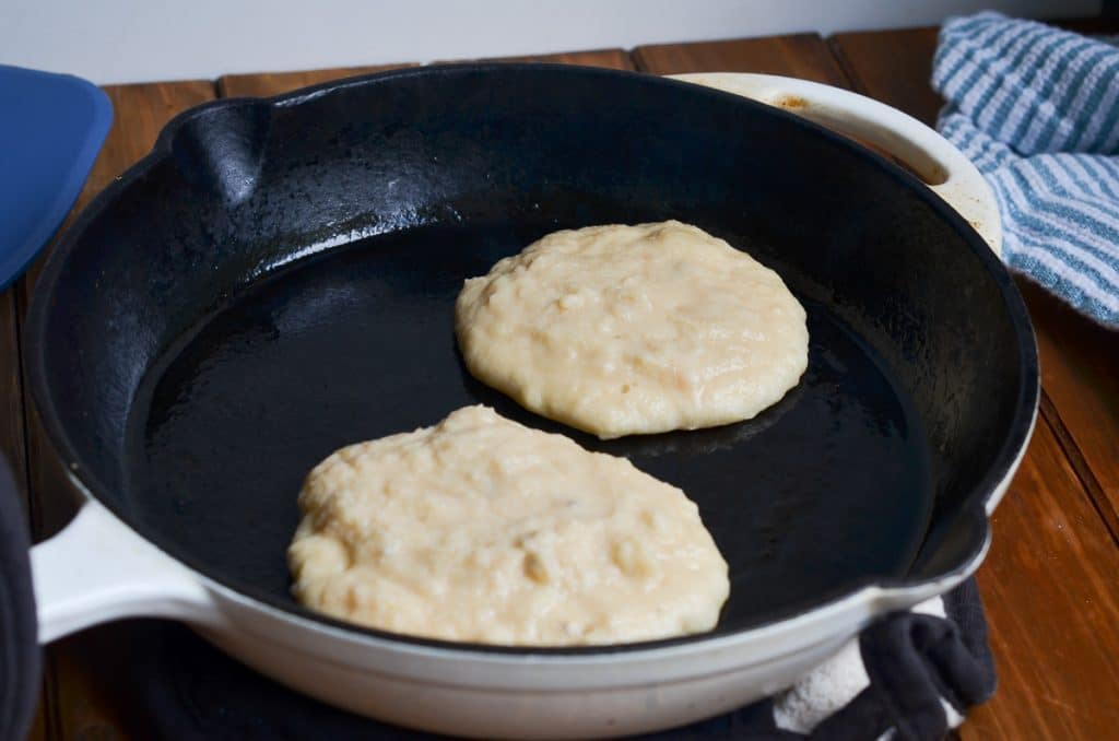 Two pancakes in hot cast iron skillet cooking.