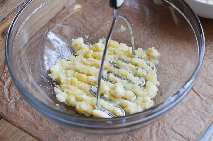 banana in bowl with potato masher.