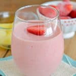 Strawberry Pineapple smoothie in a glass with a slice a strawberry. - 24 Carrot Kitchen