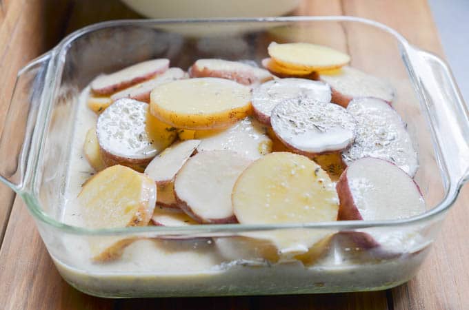 Dairy-Free milk and herb mixture poured over sliced potatoes in casserole dish.