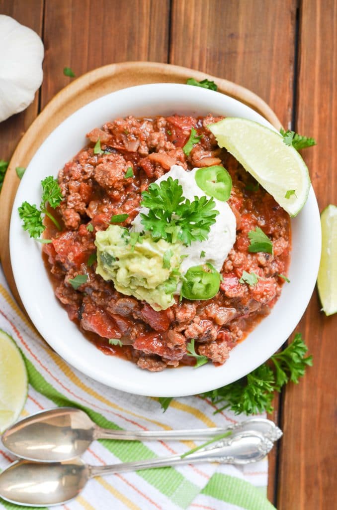 Paleo chili in a bowl with dairy-free sour cream, guacamole, wedge of lime.