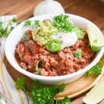 Paleo chili in a bowl with dairy-free sour cream, guacamole, wedge of lime.