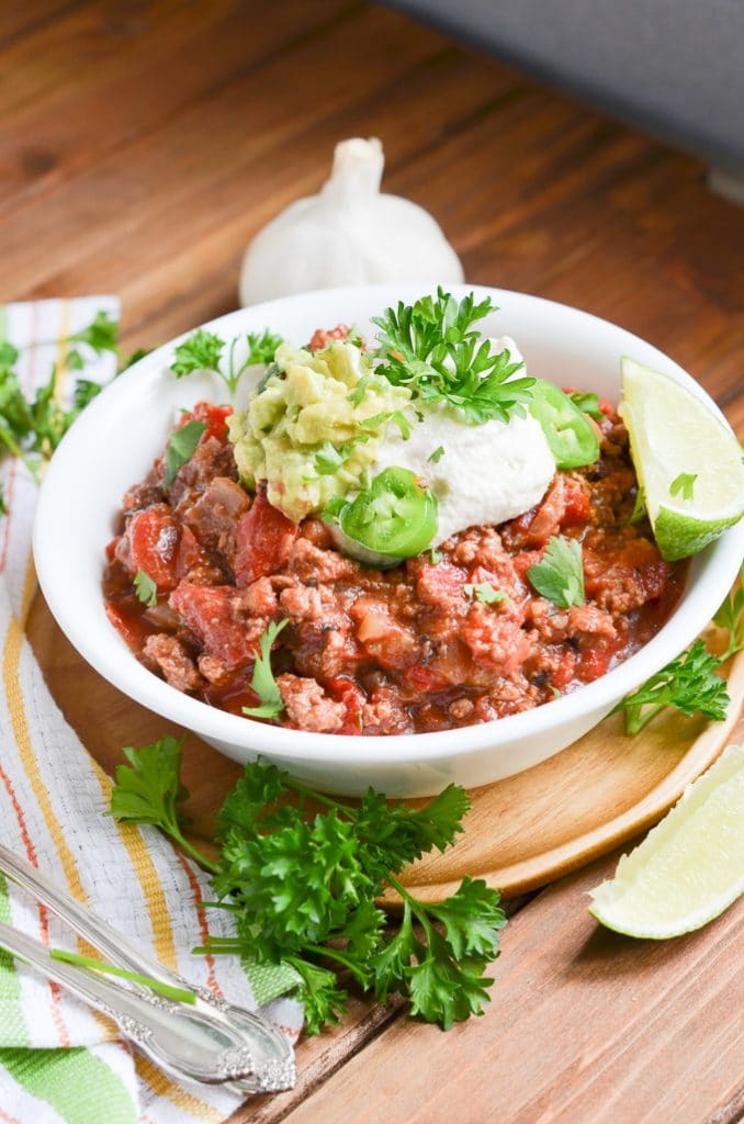 Paleo chili in a bowl with dairy-free sour cream, guacamole, wedge of lime.