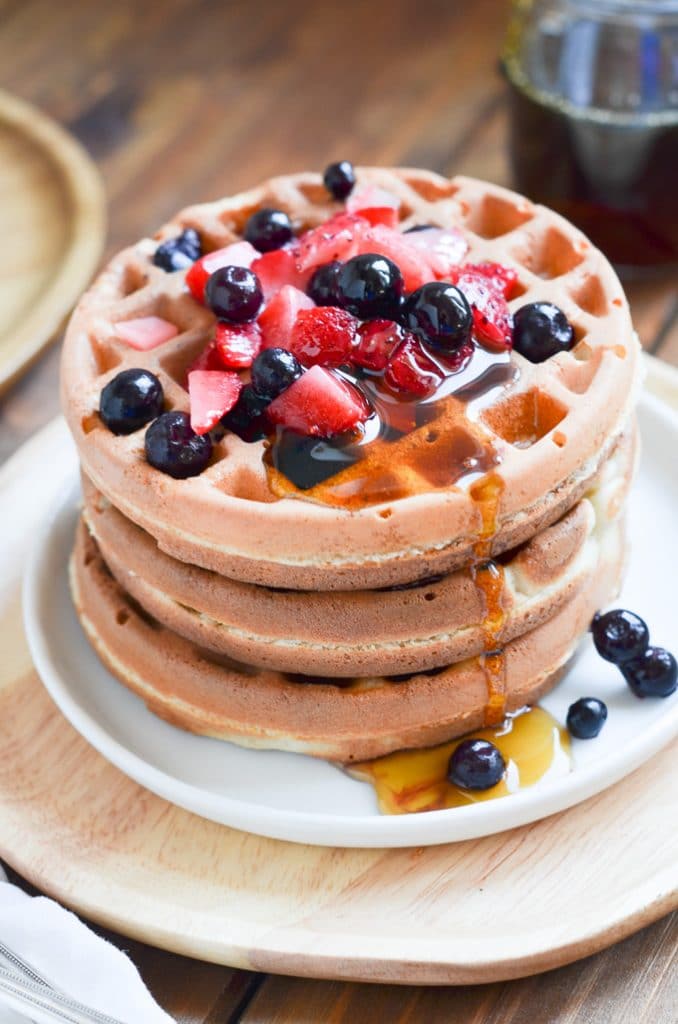 Paleo waffles on a plate with berries and maple syrup.