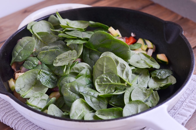 spinach is added to sauteing veggies in cast iron skillet.