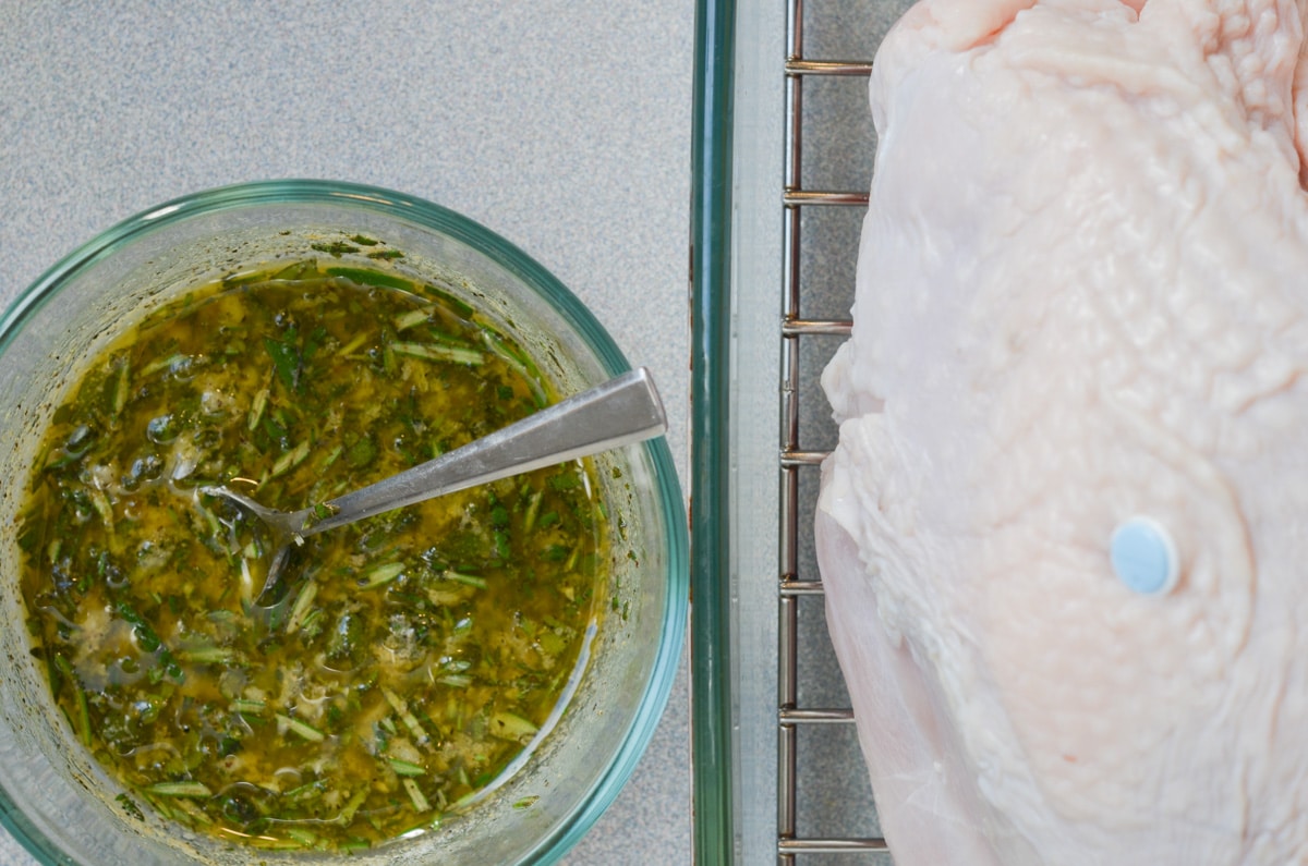 herb seasoning mix in bowl and uncooked turkey breast in roasting pan.