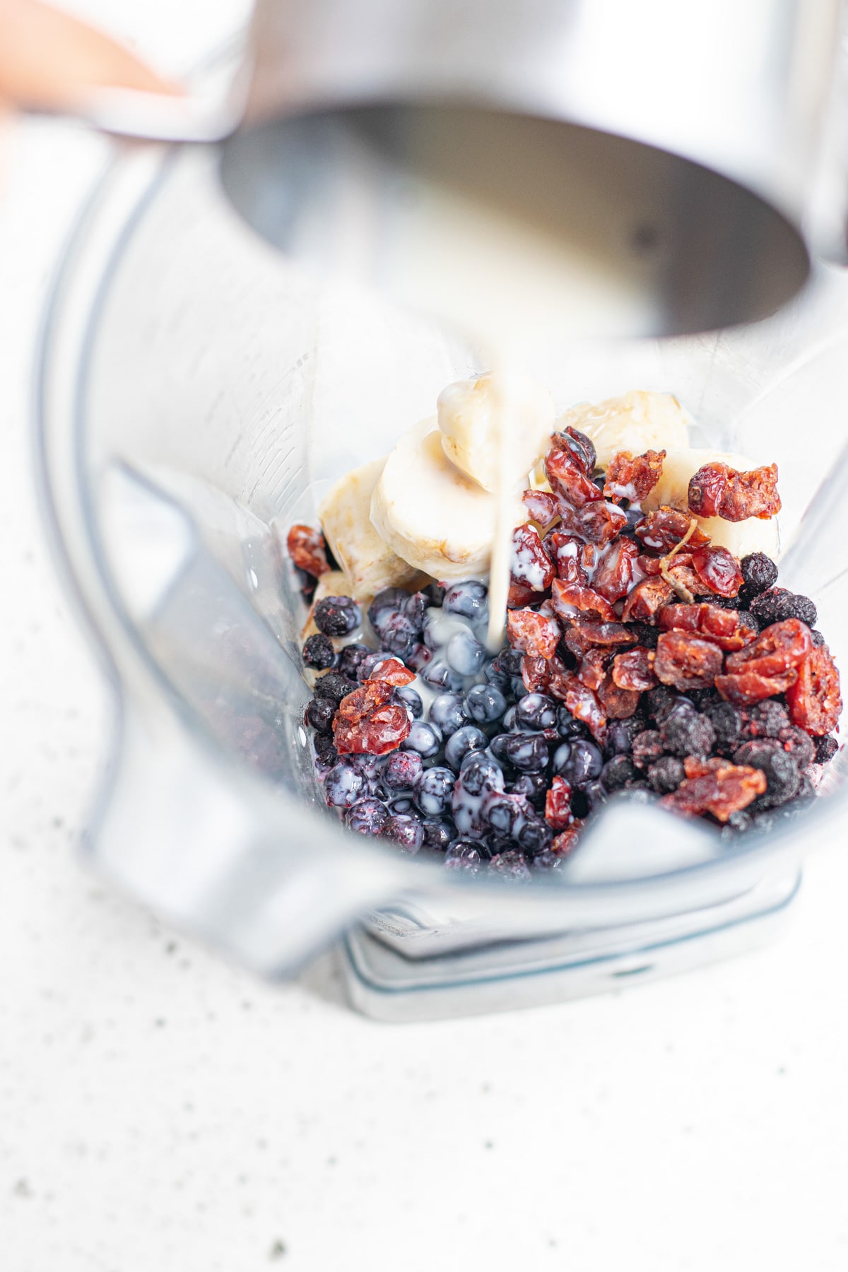 milk being poured into the blender with the other smoothie ingredients.